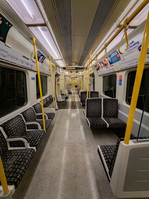 An empty passenger carriage of a train featuring clean, black fabric seats with a colorful dotted pattern arranged in pairs along the sides of the aisle. The floor is smooth, light grey, and appears s