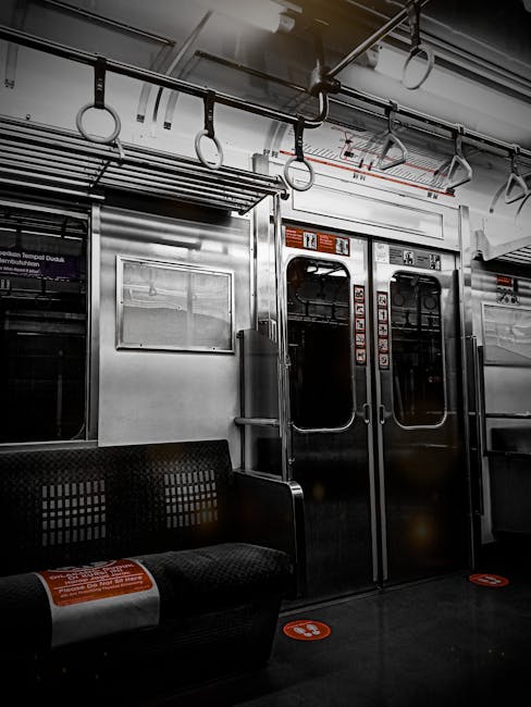 An empty passenger carriage of a train featuring clean, black fabric seats with a colorful dotted pattern arranged in pairs along the sides of the aisle. The floor is smooth, light grey, and appears s
